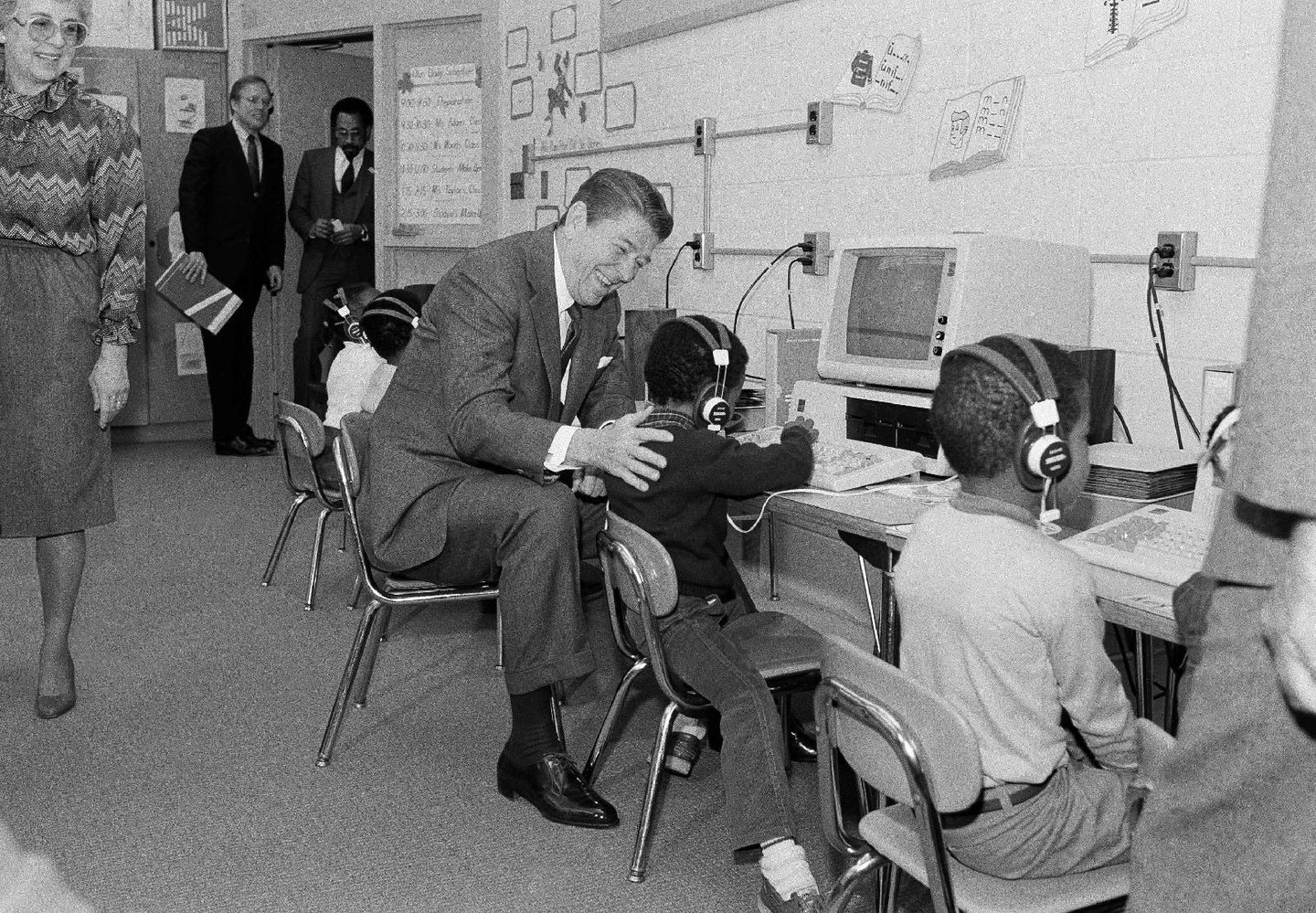 President Ronald Reagan seated beside a student using a classroom computer.